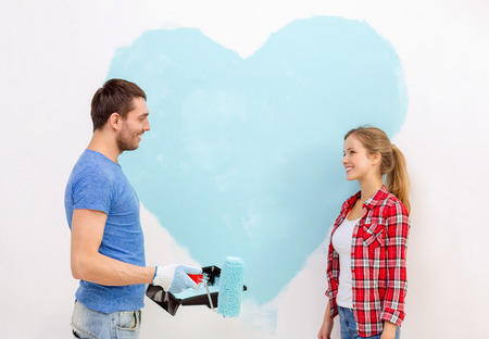 repair, building and home concept - smiling couple painting big heart on wall at homeの写真素材