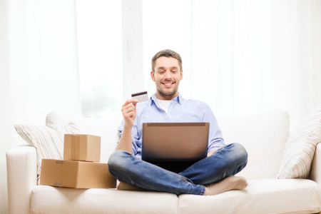 technology, home and lifestyle concept - smiling man with laptop, credit card and cardboard boxes at homeの写真素材