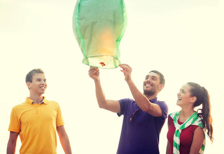 summer, holidays, vacation, happy people concept - group of friends with chinese sky lanterns on the beachの写真素材