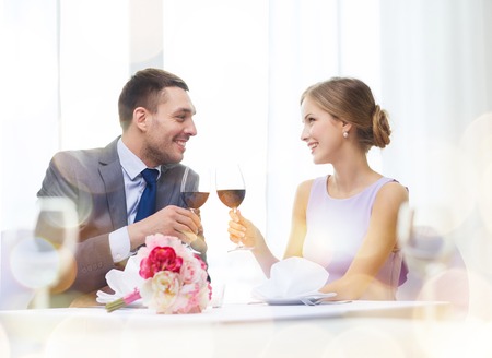 restaurant, couple and holiday concept - smiling young couple with glasses of red wine looking at each other at restaurantの写真素材