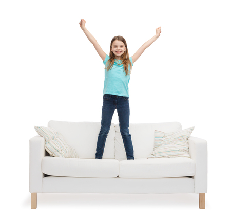 home, leisure and happiness concept - smiling little girl jumping or dancing on sofaの写真素材