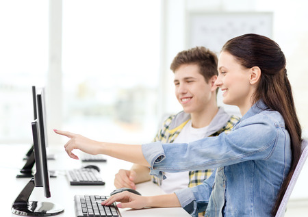 education, technology and school concept - two smiling students in computer class, girl pointing...