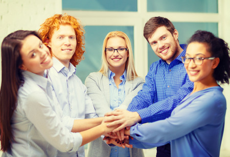 business, office, gesture and startup concept - smiling creative team with hands on top of each...