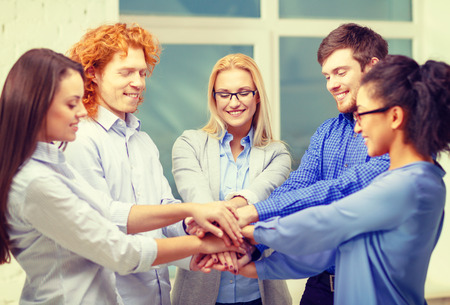 business, office, gesture and startup concept - smiling creative team with hands on top of each other sitting in officeの写真素材