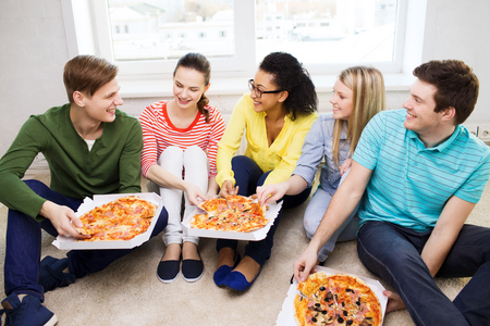 food, leisure and happiness concept - five smiling teenagers eating pizza at homeの写真素材