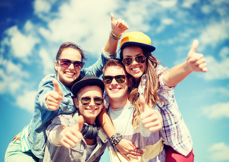 summer holidays and teenage concept - group of smiling teenagers in sunglasses hanging outside and showing thumbs up