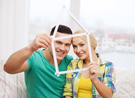moving, home and couple concept - smiling couple with house from measuring tape at new homeの写真素材