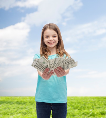 money, finances and people concept - smiling little girl giving dollar cash moneyの写真素材