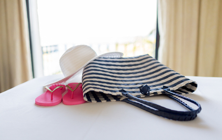 vacation, holiday and travel concept - close-up of beach bag, straw hat and flip-flop on hotel bedの写真素材