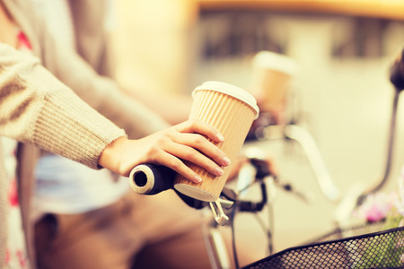 summer holidays, bikes, love, relationship and dating concept - closeup of woman hand holding coffee and riding bicycleの写真素材