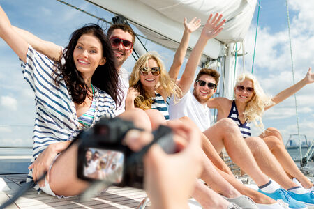 vacation, travel, sea, friendship and people concept - smiling friends sitting on yacht deck and photographingの写真素材
