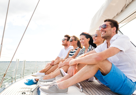 vacation, travel, sea, friendship and people concept - smiling friends sitting on yacht deckの写真素材