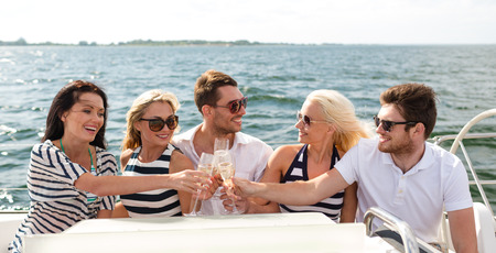 vacation, travel, sea, friendship and people concept - smiling friends with glasses of champagne on yachtの写真素材