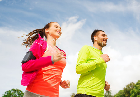 fitness, sport, friendship and lifestyle concept - smiling couple with earphones running outdoorsの写真素材