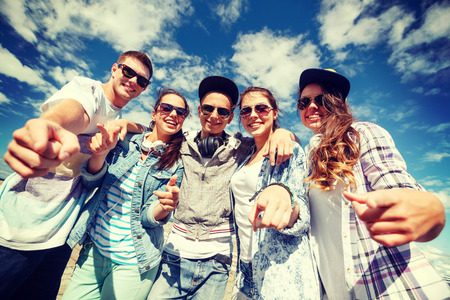 summer holidays and teenage concept - group of smiling teenagers in sunglasses hanging outside pointing finger at youの写真素材