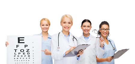 healthcare, vision and medicine concept - smiling female eye doctors and nurses with eye exam chart,...