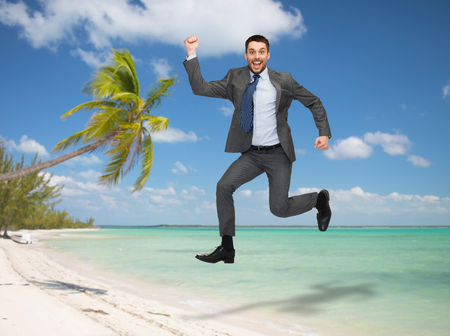 business, education and people concept - smiling happy businessman jumping over tropical beach backgroundの写真素材