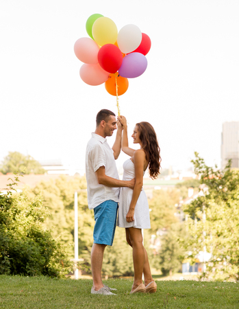 love, wedding, summer, dating and people concept - smiling couple wearing sunglasses with balloons hugging in parkの写真素材