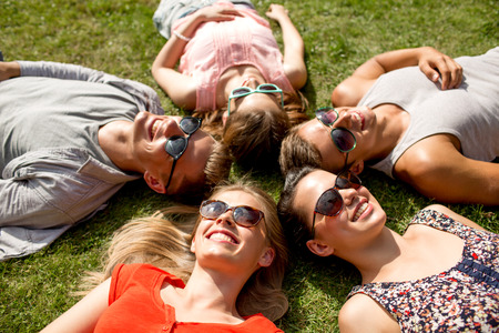 friendship, leisure, summer and people concept - group of smiling friends lying on grass in circle outdoorsの写真素材