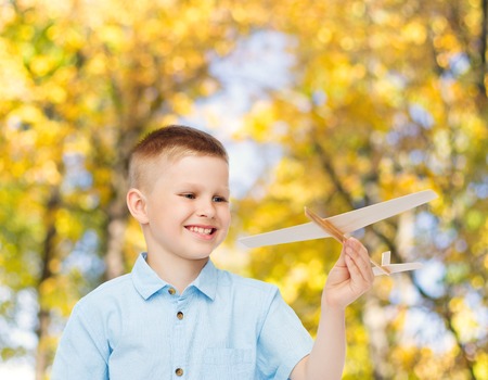 dreams, future, hobby, season and childhood concept - smiling little boy holding wooden airplane model in his hand over autumn park backgroundの写真素材
