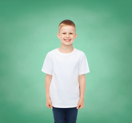 happiness, childhood, school education, advertisement and people concept - smiling little boy in white t-shirt over green board backgroundの写真素材