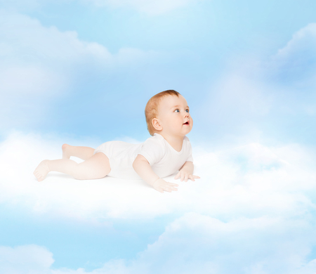 child and toddler concept - smiling baby lying on cloud and looking upの写真素材
