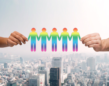 community, unity and teamwork concept - close up of multiracial couple hands holding paper chain gay people cutout over city backgroundの写真素材
