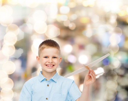 dreams, future, hobby, holidays and childhood concept - smiling little boy holding wooden airplane model in his hand over sparkling backgroundの写真素材