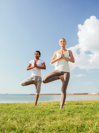 fitness, sport, friendship and lifestyle concept - smiling couple making yoga exercises outdoorsの写真素材