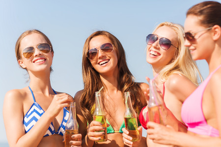 summer vacation, holidays, travel and people concept - group of smiling young women sunbathing and drinking on beachの写真素材
