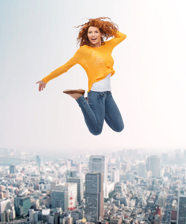 happiness, freedom, movement and people concept - smiling young woman jumping in air over city backgroundの写真素材