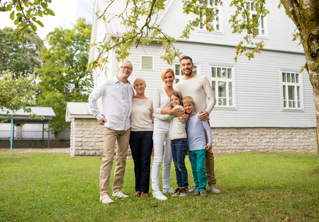 family, happiness, generation, home and people concept - happy family standing in front of house...