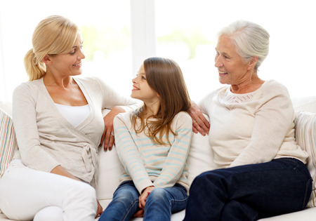 family, happiness, generation and people concept - smiling mother, daughter and grandmother sitting on couch at homeの写真素材