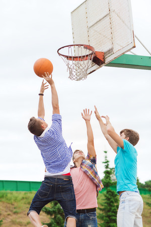 summer vacation, holidays, games and friendship concept - group of teenagers playing basketball outdoorsの写真素材