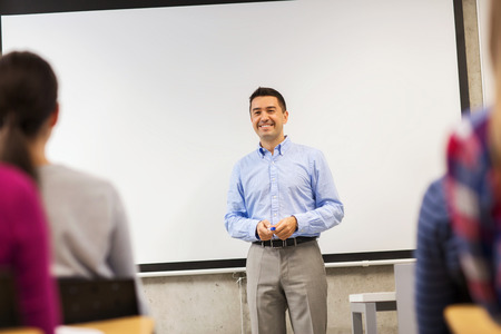 education, high school, teamwork and people concept - smiling teacher standing in front of white board and students in classroomの写真素材