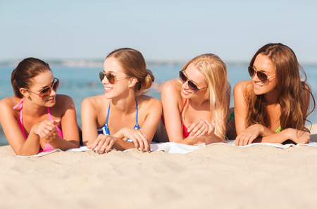 summer vacation, holidays, travel and people concept - group of smiling young women in sunglasses lying on beachの写真素材