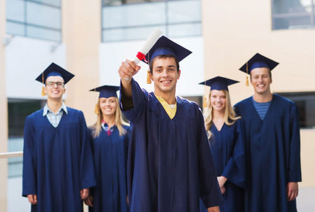 education, graduation and people concept - group of smiling students in mortarboards and gowns with diploma outdoorsの写真素材