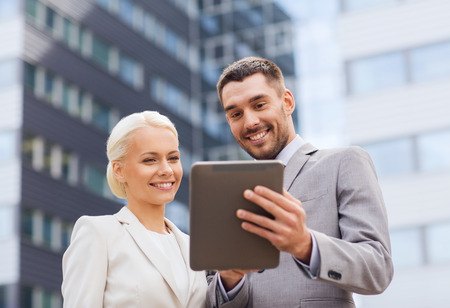 business, partnership, technology and people concept - smiling businessman and businesswoman with tablet pc computer over office buildingの写真素材