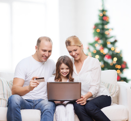 family, holidays, shopping, technology and people - happy family with laptop computer and credit card over living room and christmas tree backgroundの写真素材