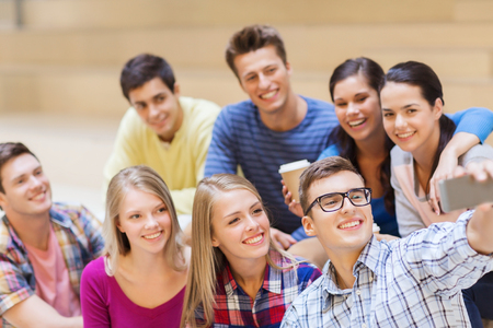 education, friendship, drinks, technology and people concept - group of smiling students with smartphone and paper coffee cup taking selfie at schoolの写真素材