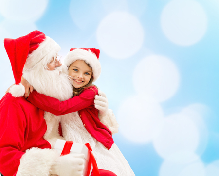 holidays, christmas, childhood and people concept - smiling little girl hugging with santa claus over blue lights backgroundの写真素材