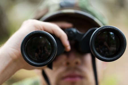 hunting, war, army and people concept - close up of young soldier, ranger or hunter with binocular observing forestの写真素材