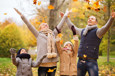 family, childhood, season and people concept - happy family playing with autumn leaves in parkの写真素材