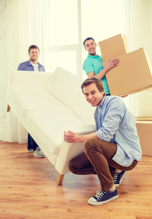 moving, real estate and friendship concept - smiling male friends with sofa and boxes at new homeの写真素材