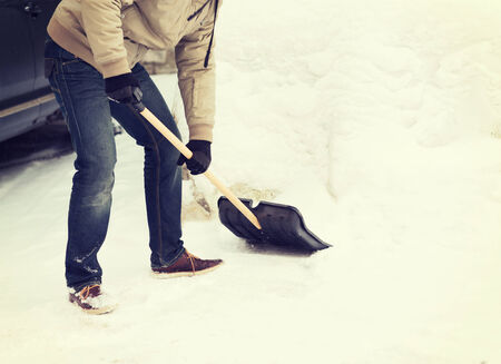 winter and cleaning concept - closeup of man shoveling snow from driveway