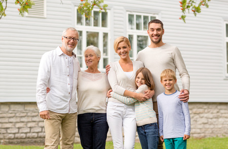 family, happiness, generation, home and people concept - happy family standing in front of house outdoorsの写真素材