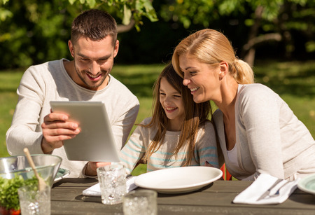 family, happiness, generation, home and people concept - happy family sitting at table with tablet pc computer outdoorsの写真素材