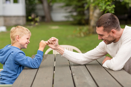 family, happiness, generation, home and people concept - happy father and son doing arm wrestling outdoorsの写真素材