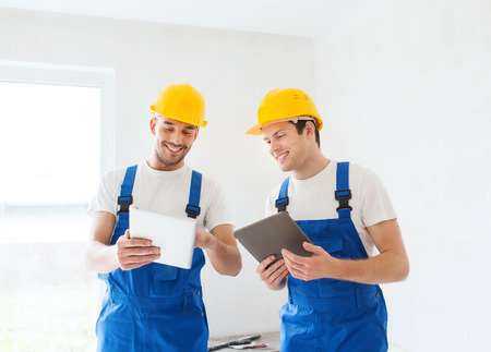 building, renovation, technology, electricity and people concept - two builders with tablet pc...
