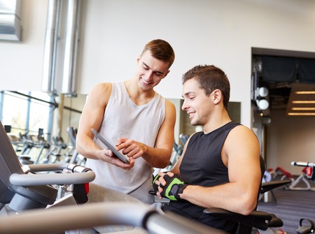 sport, fitness, equipment, technology and people concept - men with tablet pc computer exercising on...